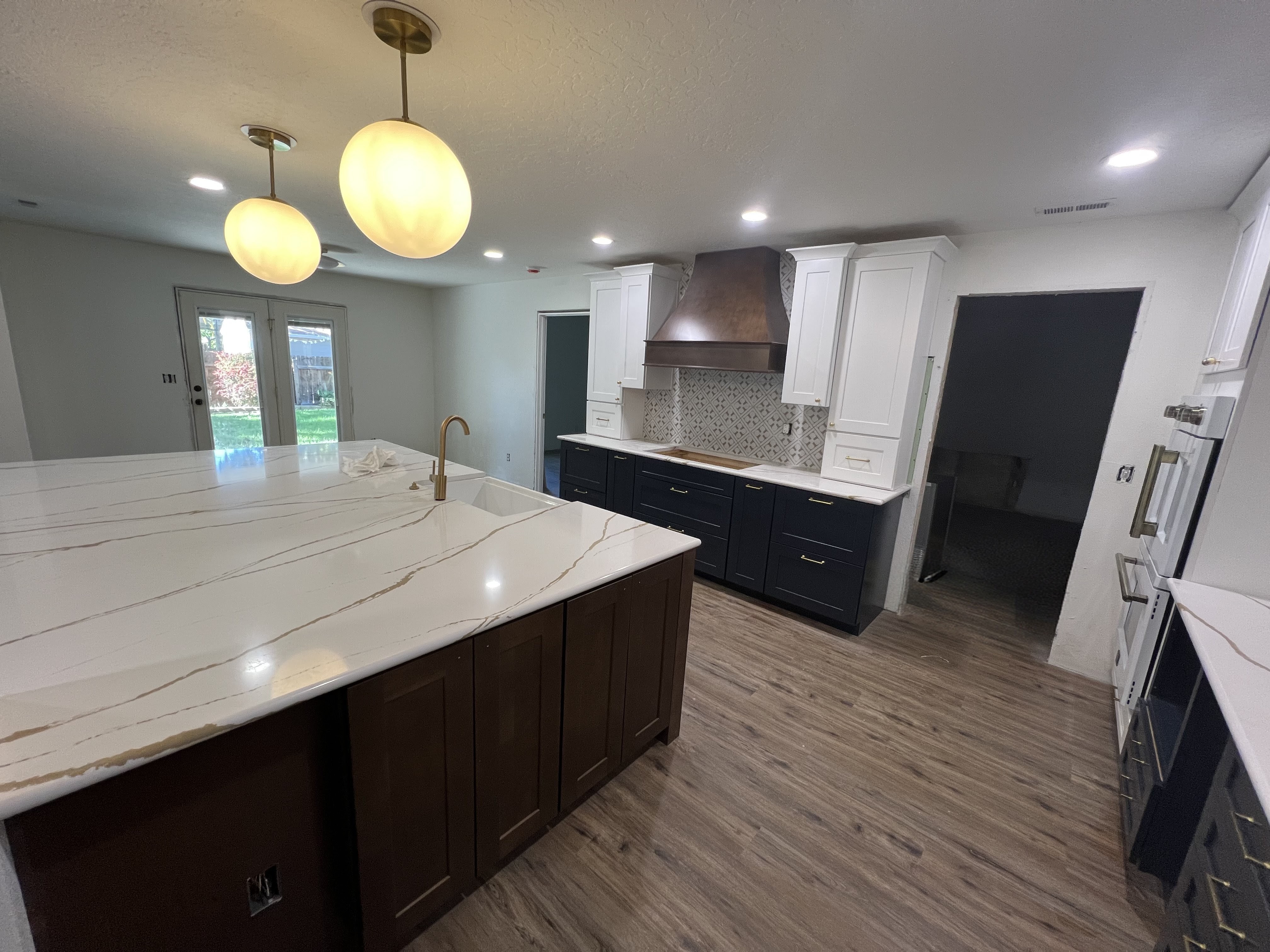 Kitchen after the KB Designs remodel with navy cabinetry, marble waterfall island and brass fixtures