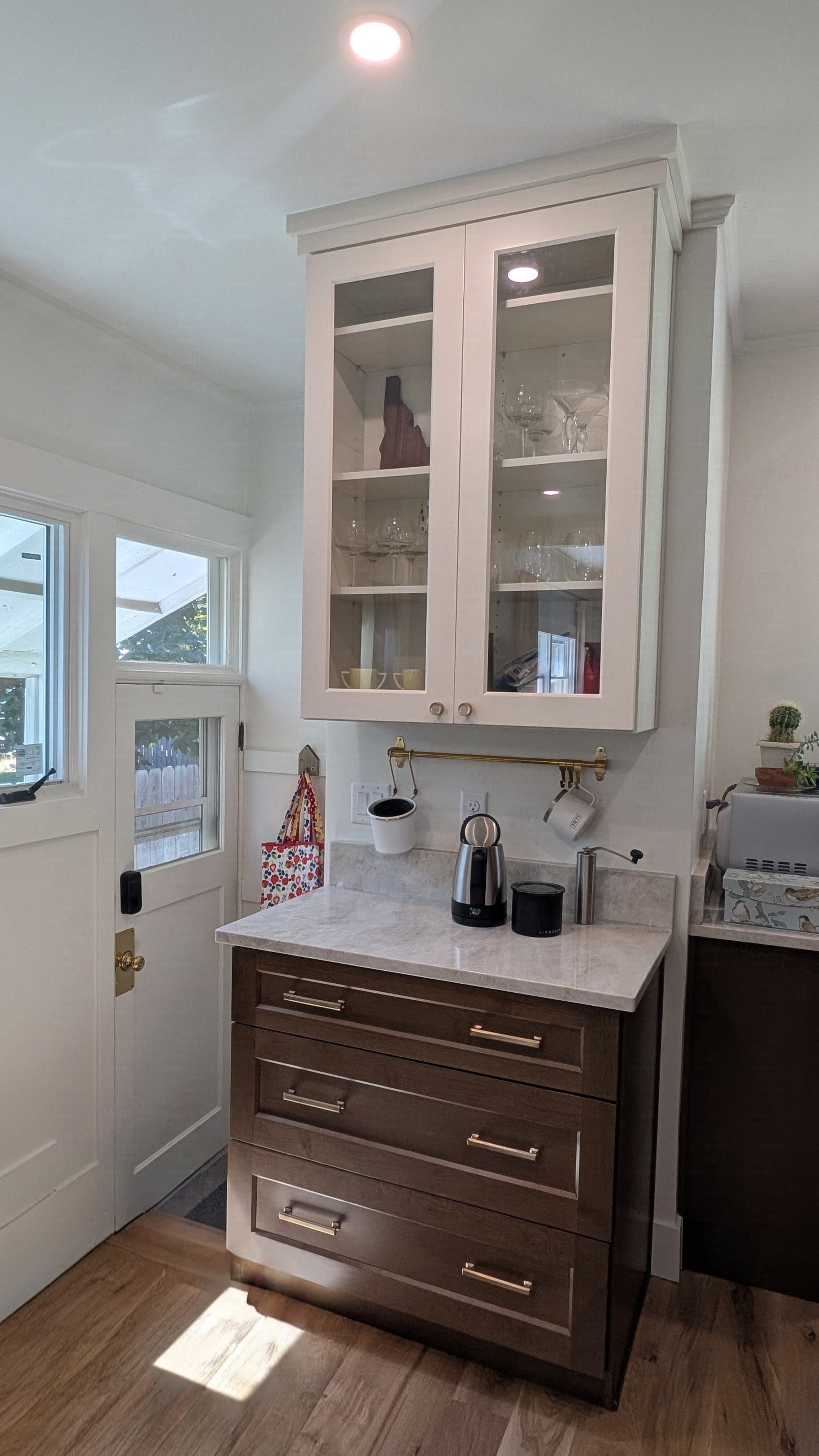 Remodeled butler pantry and coffee bar with white glass-front uppers, dark wood base and brass rail