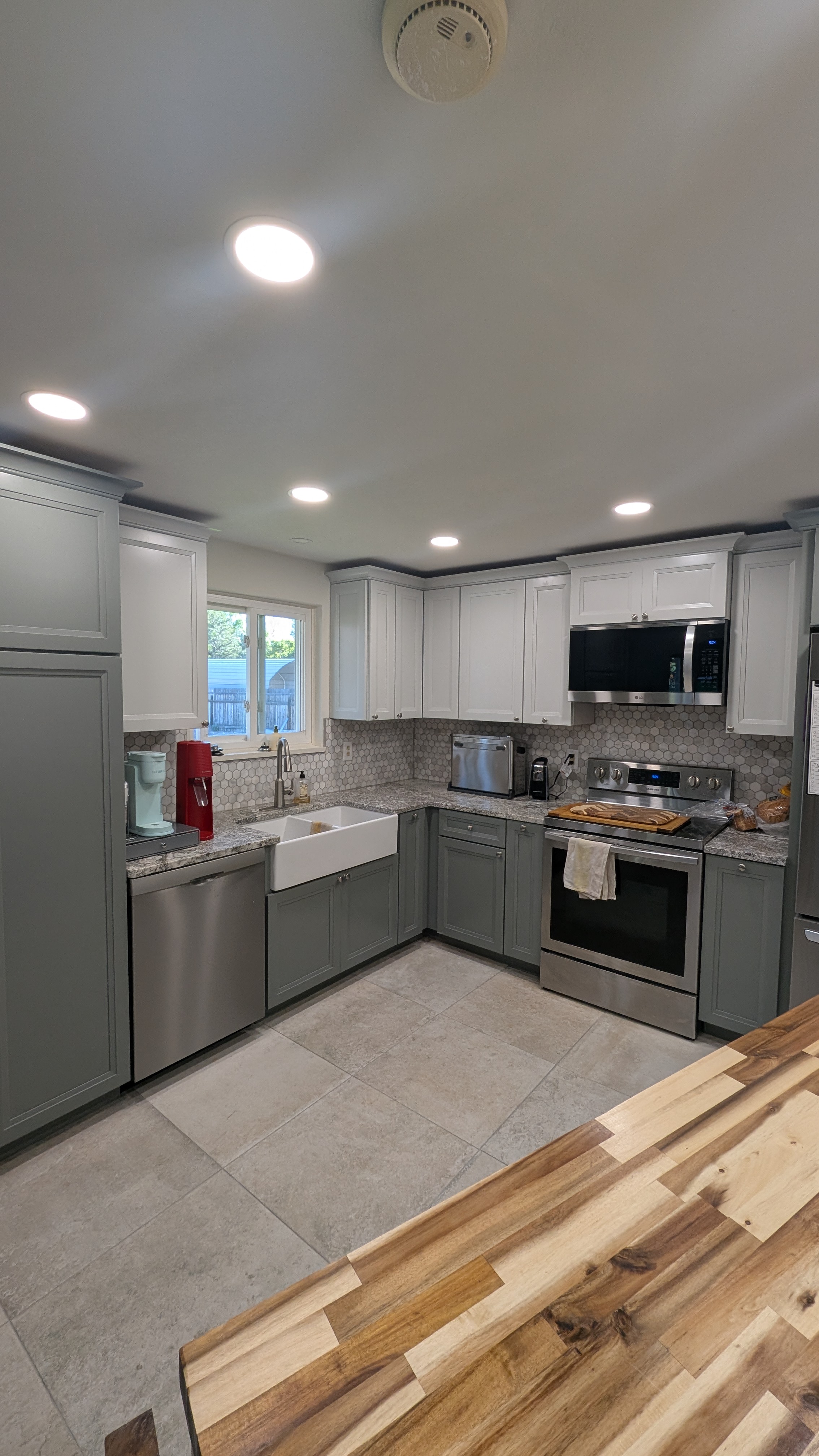 Remodeled two-tone kitchen with white upper cabinets, gray lowers, granite counters, farmhouse sink, and hexagon mosaic backsplash
