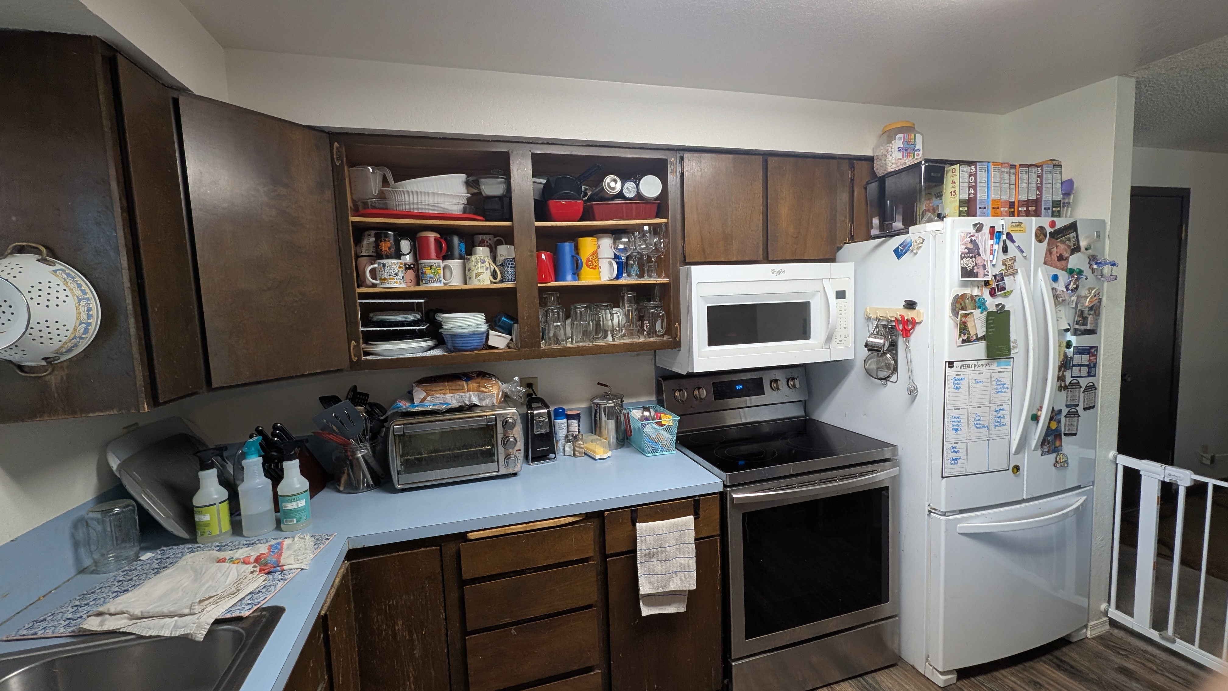 Dated kitchen with dark wood cabinets, blue laminate counters, and cluttered open shelving before remodel