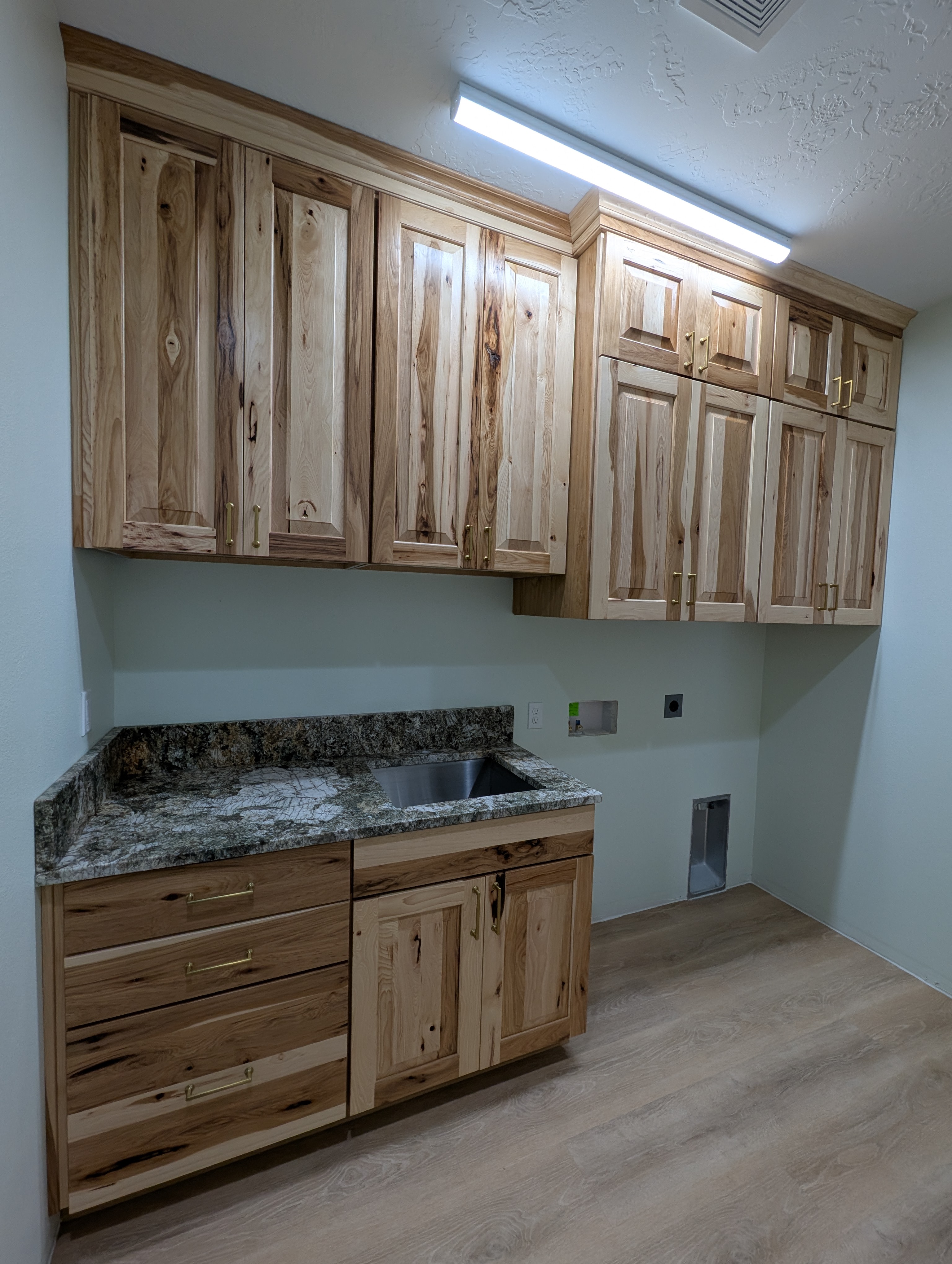 Remodeled laundry room with hickory cabinetry, granite counter with sink and wood-look floors