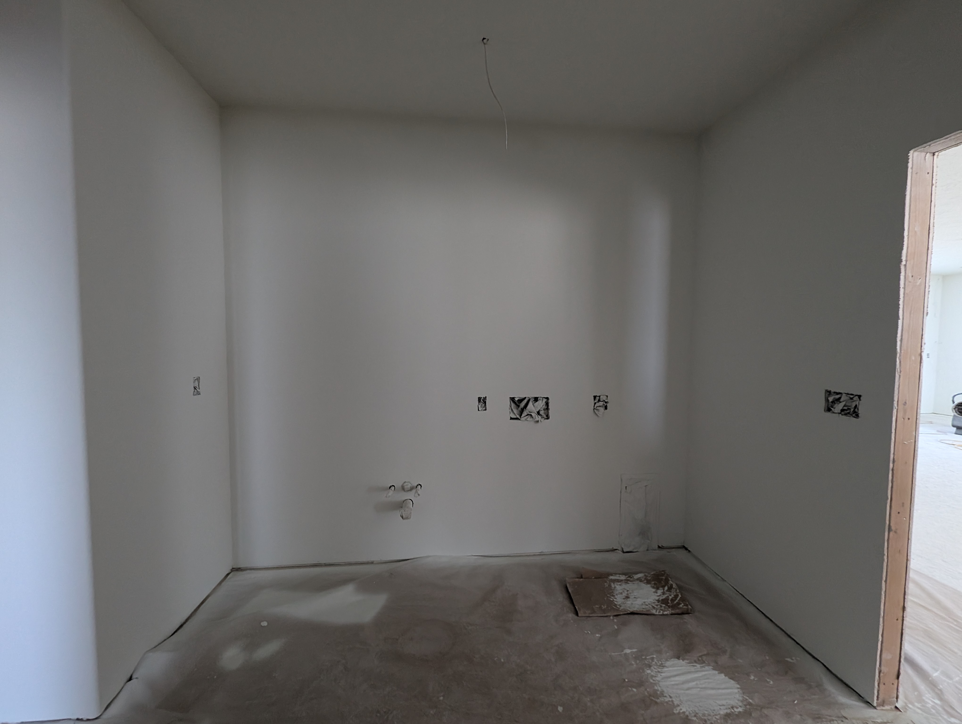 Gutted utility room with bare drywall and concrete floor before remodel