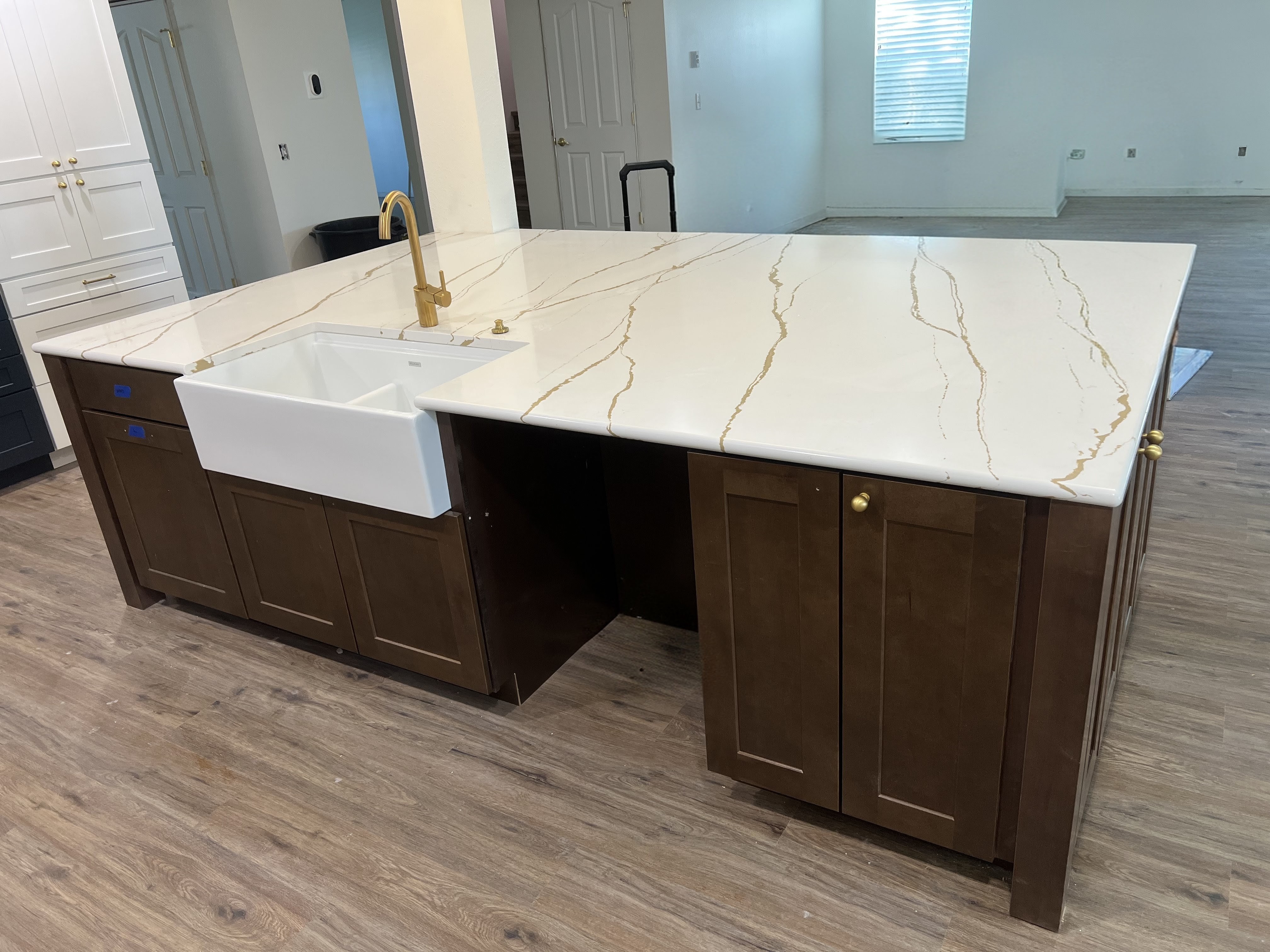 Remodeled kitchen island with espresso shaker cabinets, gold-veined white quartz waterfall counter, farmhouse apron sink and brass faucet