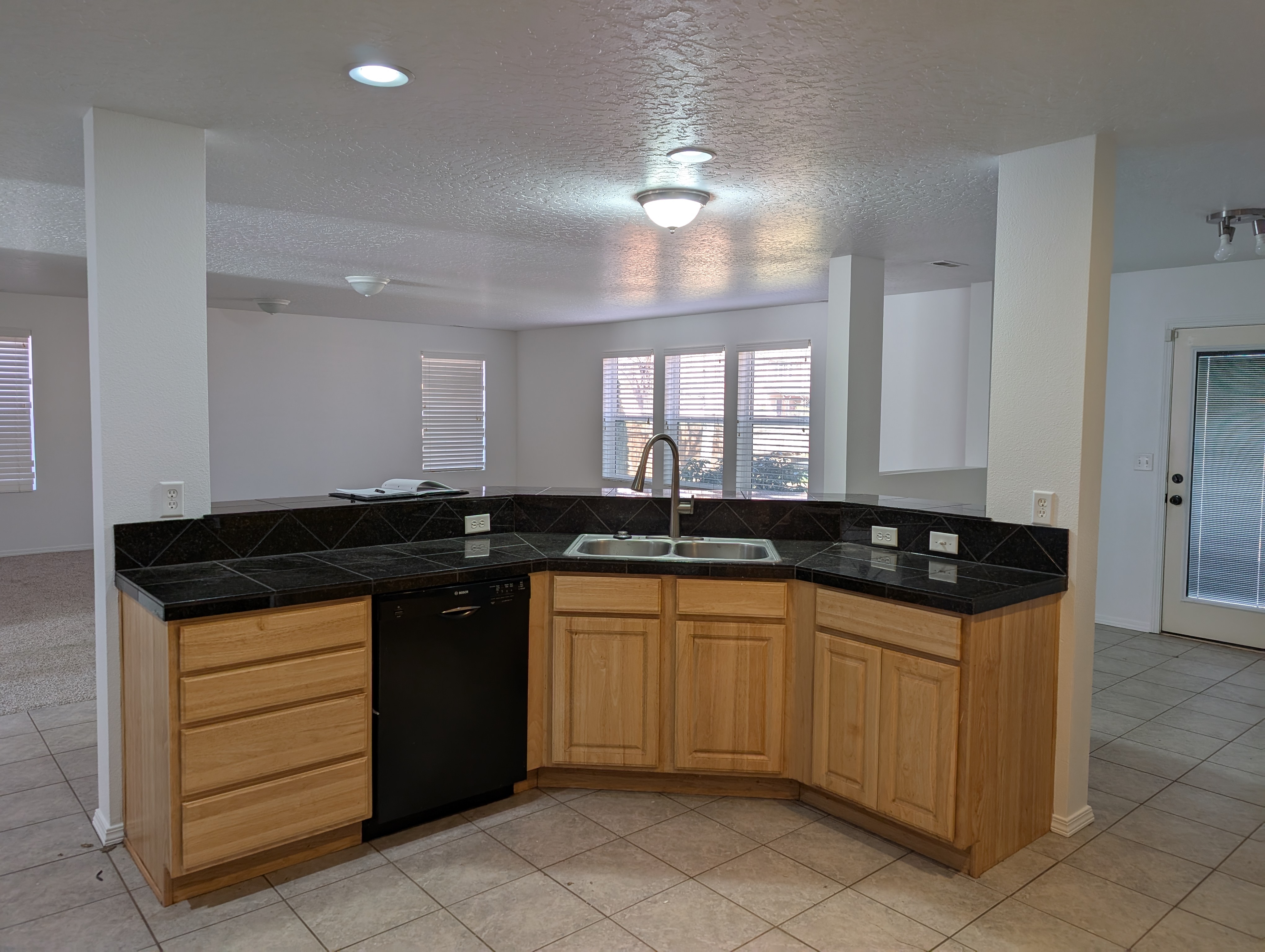 Dated peninsula kitchen with honey-oak cabinets and black diagonal tile counters before remodel