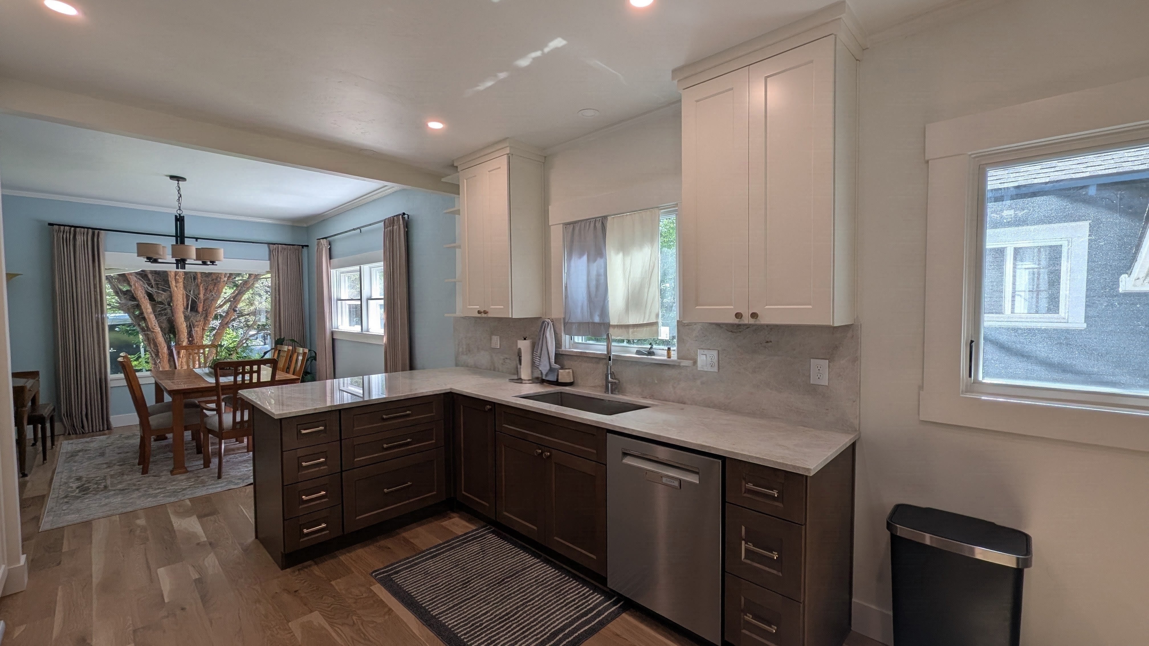 Remodeled open kitchen with cream shaker uppers, espresso lower cabinets, quartz counters and full-height backsplash opening to a dining room