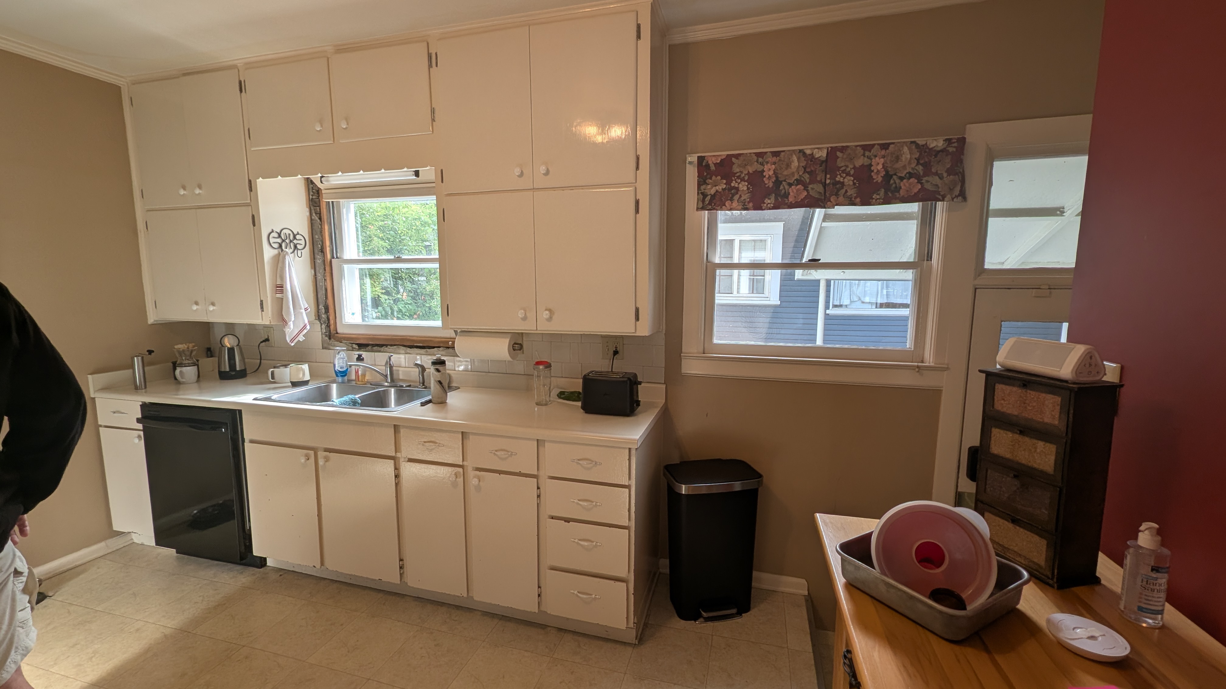Dated kitchen sink wall with glossy white flat-panel cabinets, laminate counters and floral valance before remodel