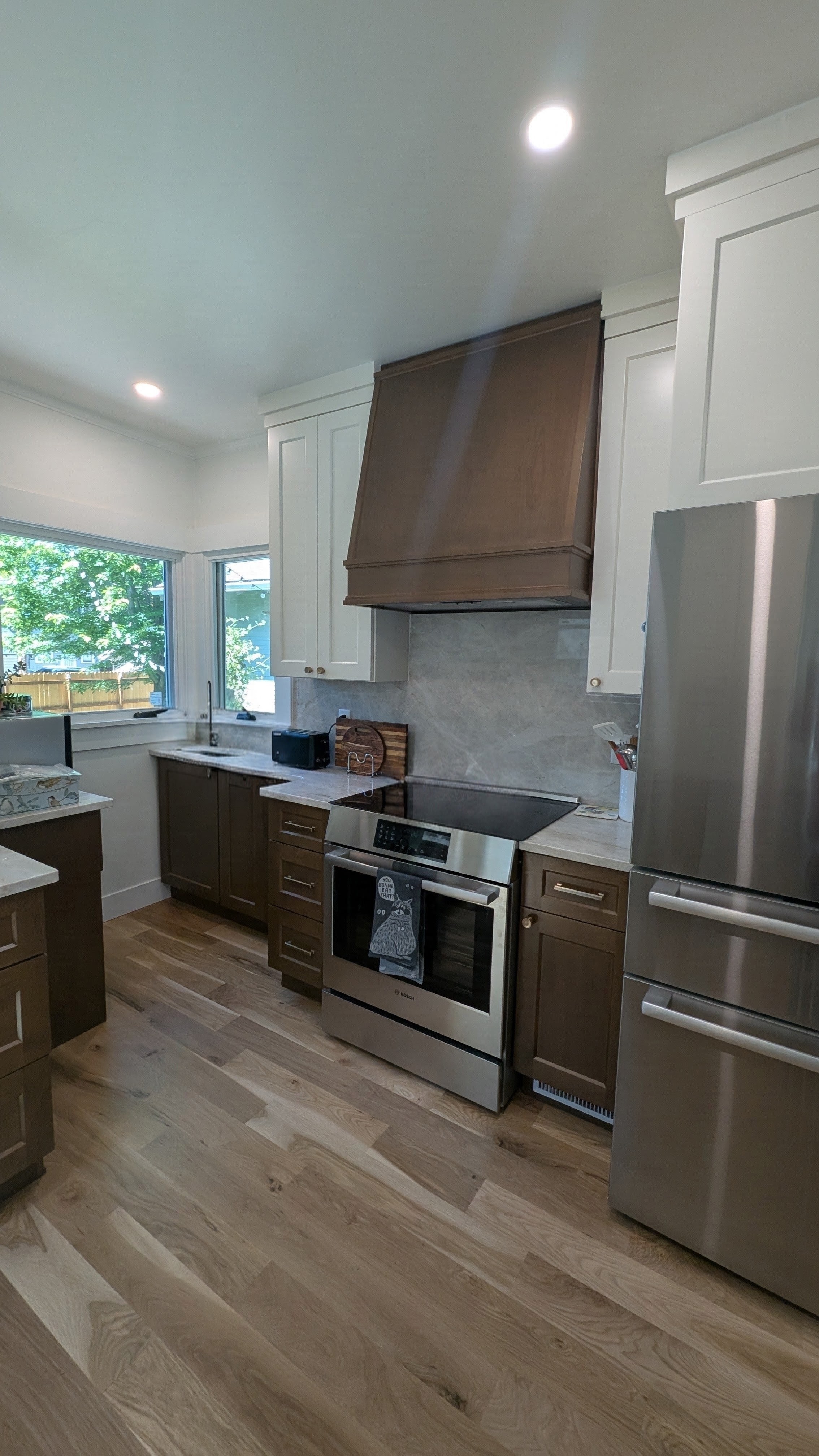 Remodeled galley kitchen with stained wood shaker cabinets, custom wood range hood, quartz counters, stainless appliances and hardwood floors