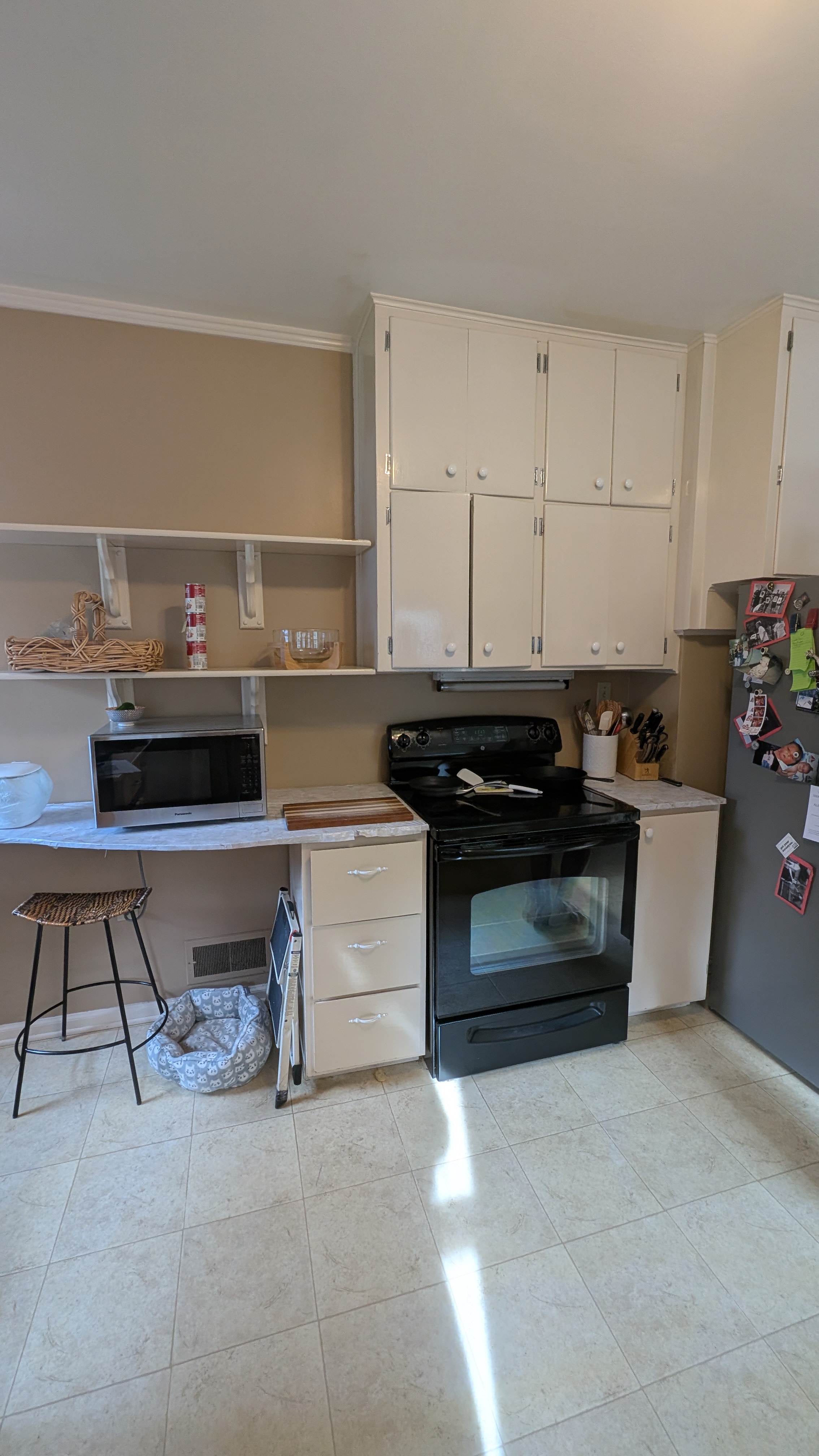 Dated stove wall with glossy white flat-panel cabinets, open bracket shelving and a black electric range before remodel