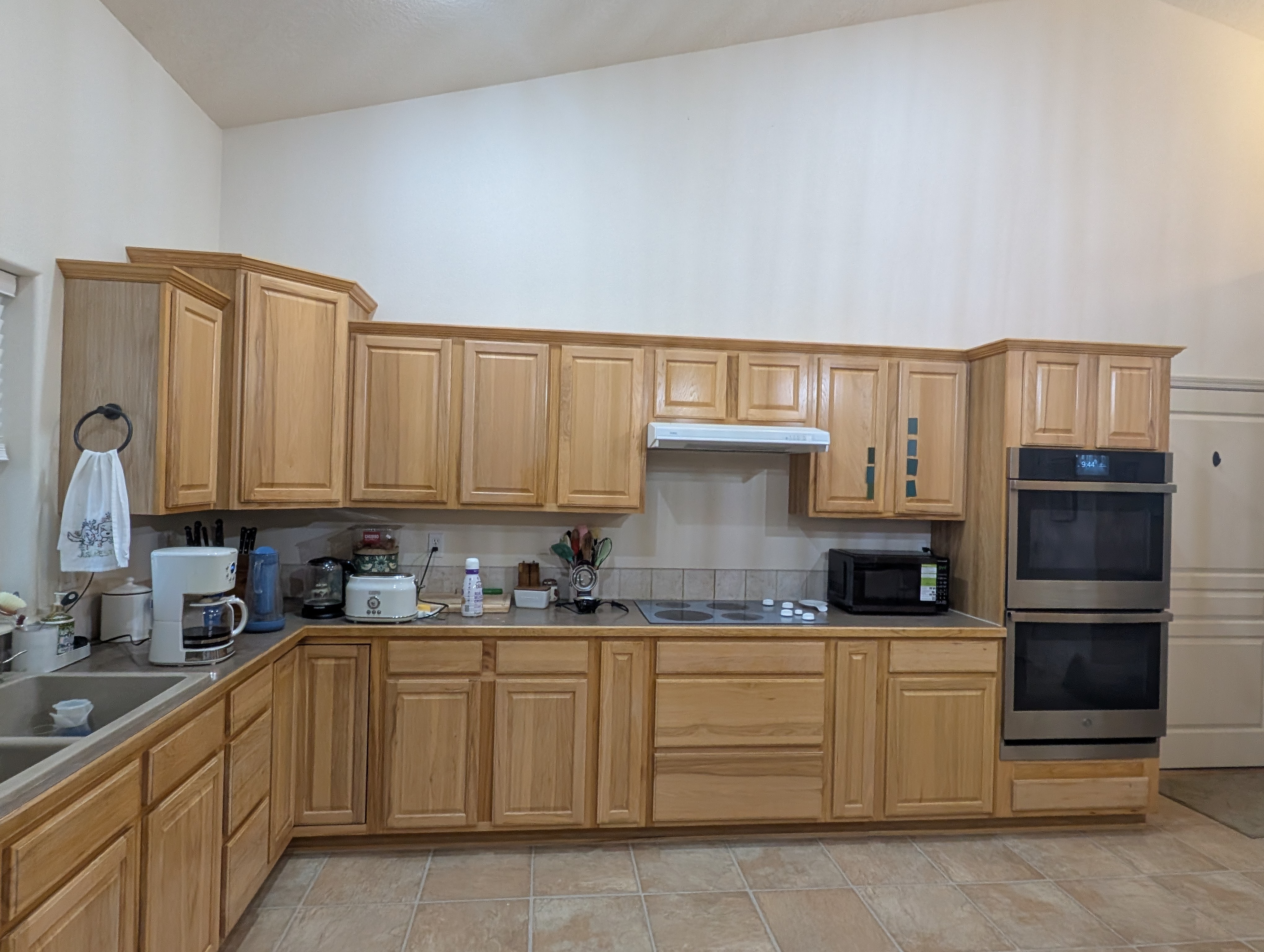 Dated L-shaped kitchen with honey-oak raised-panel cabinets, tan laminate counters and beige tile floor before remodel