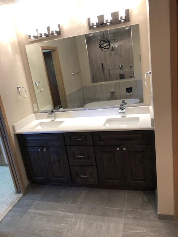 Dark-wood double vanity bathroom with white counters and a large mirror reflecting the shower