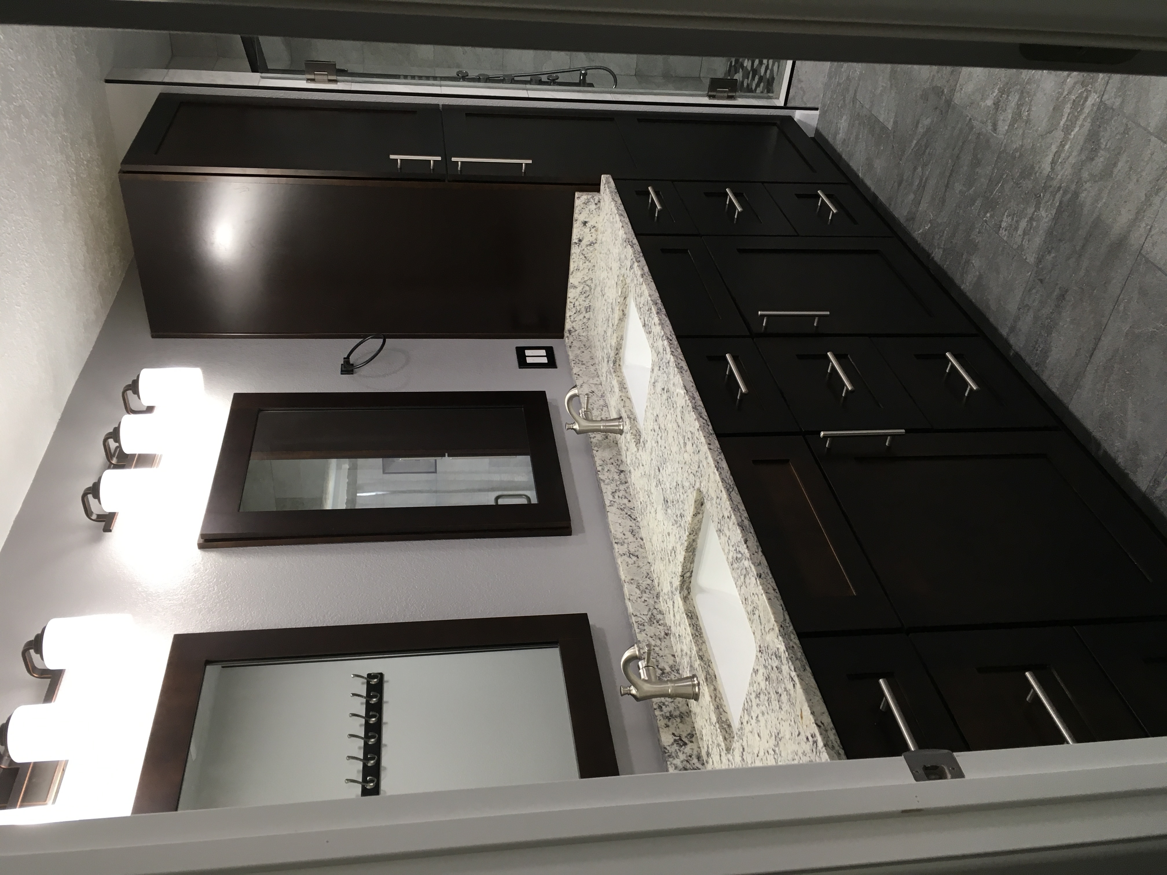 Galley bathroom with espresso cabinetry, granite counters, a tall linen cabinet and a glass shower