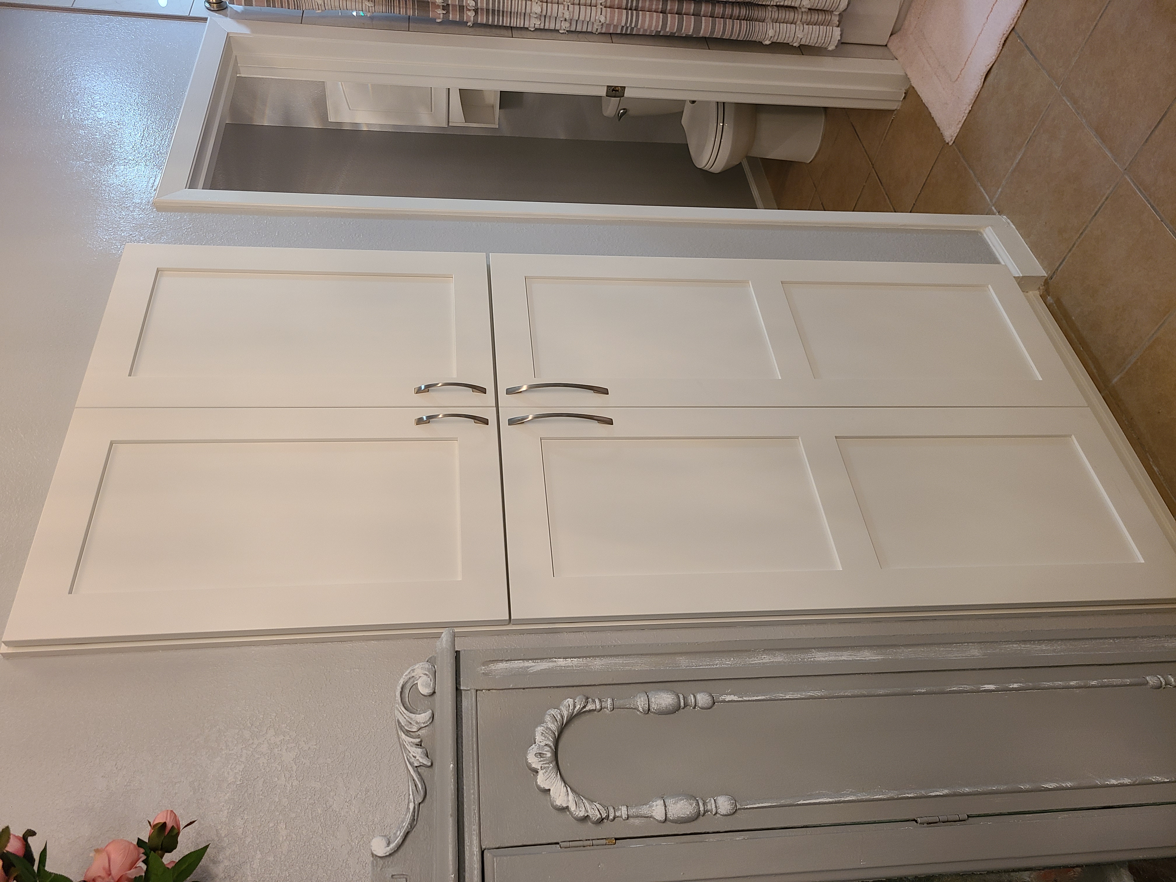 Tall white shaker linen tower cabinet in a bathroom beside a painted antique cabinet