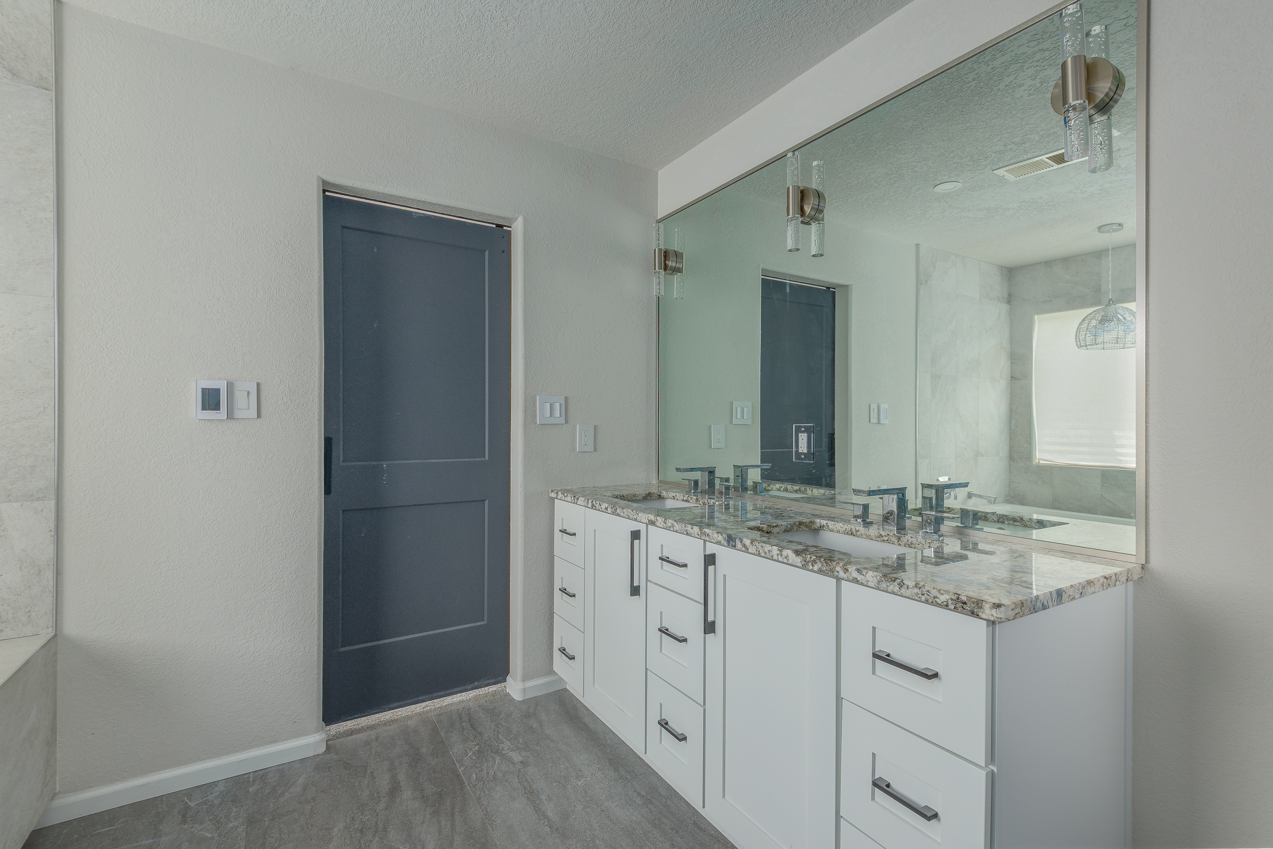 Modern master bath with white vanity, granite counters, a large mirror and a navy sliding barn door