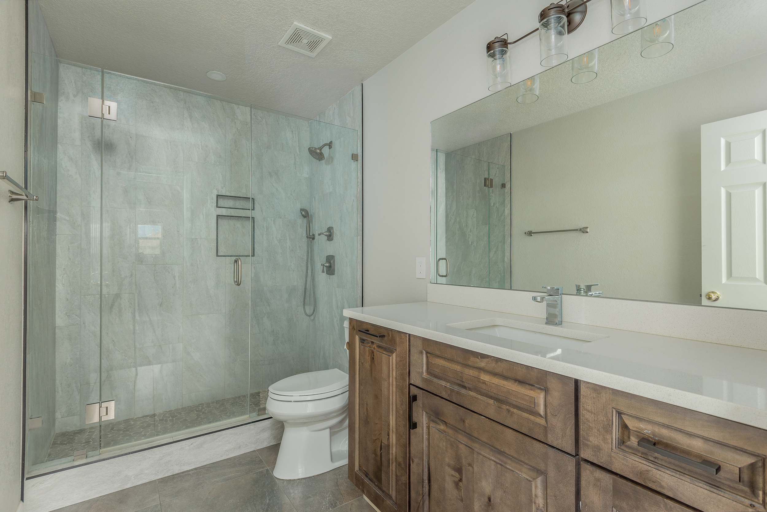 Guest bath with a rustic stained-wood vanity, white quartz counter and a marble-tiled glass shower