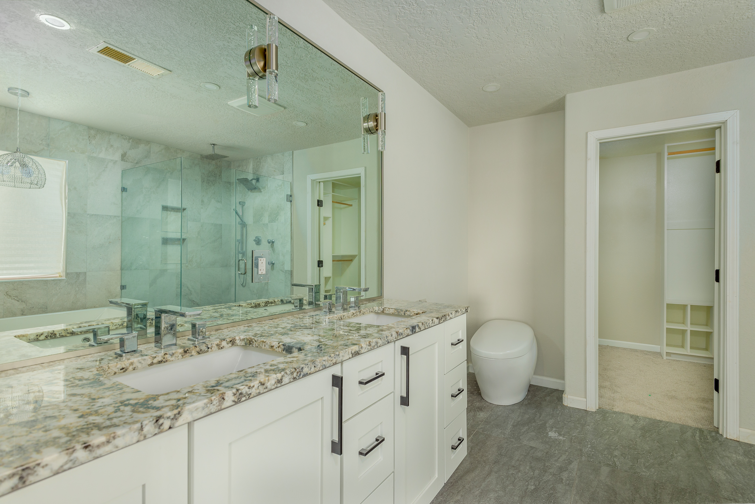 Bright master bath with white vanity, granite counters, glass shower and a soaking tub