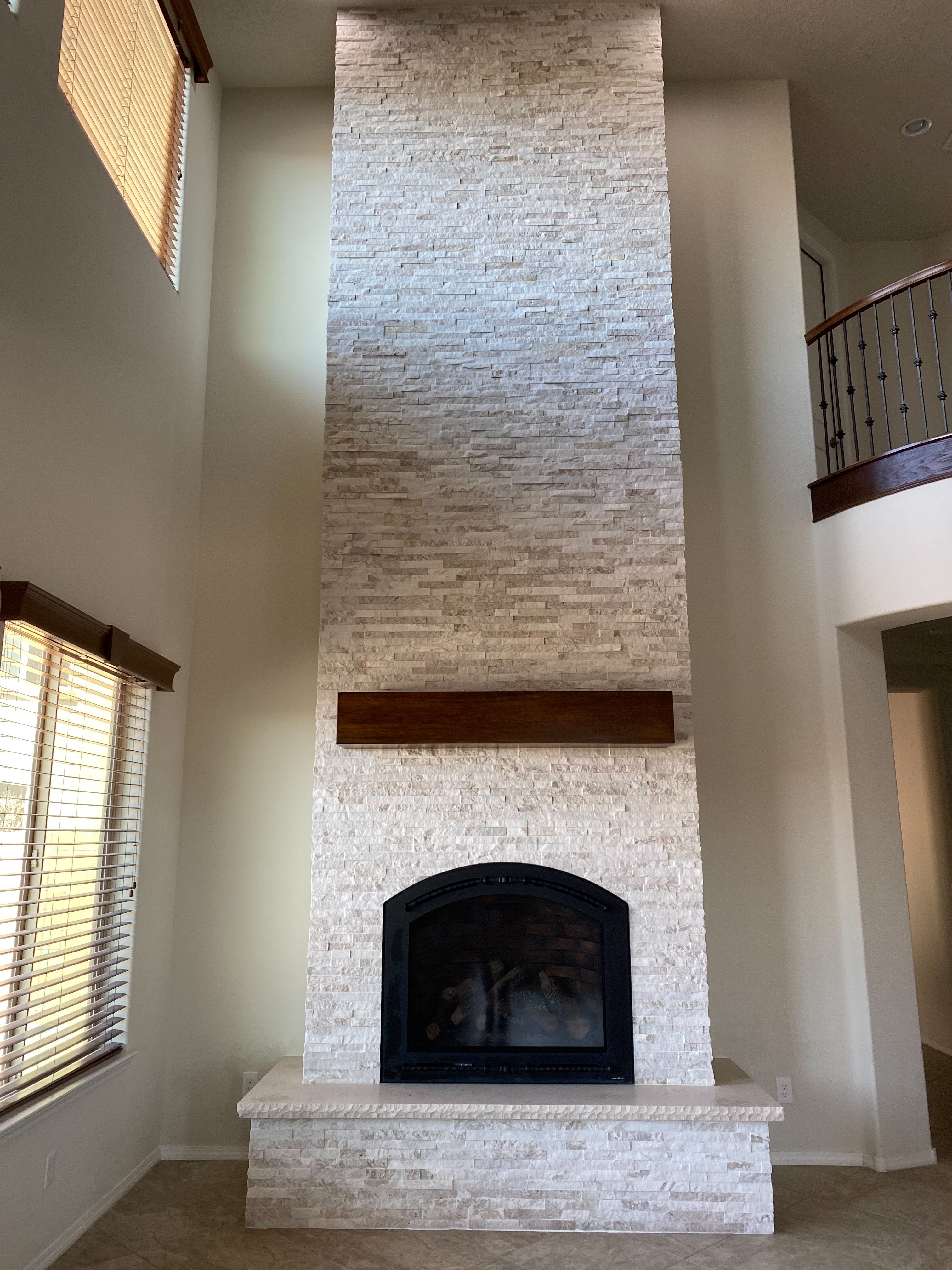 Dramatic floor-to-ceiling stacked stone fireplace with a wood mantel in a two-story great room