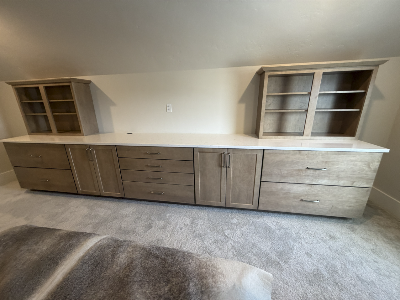 Long gray-stained built-in storage wall with open display hutches, drawers and a quartz counter