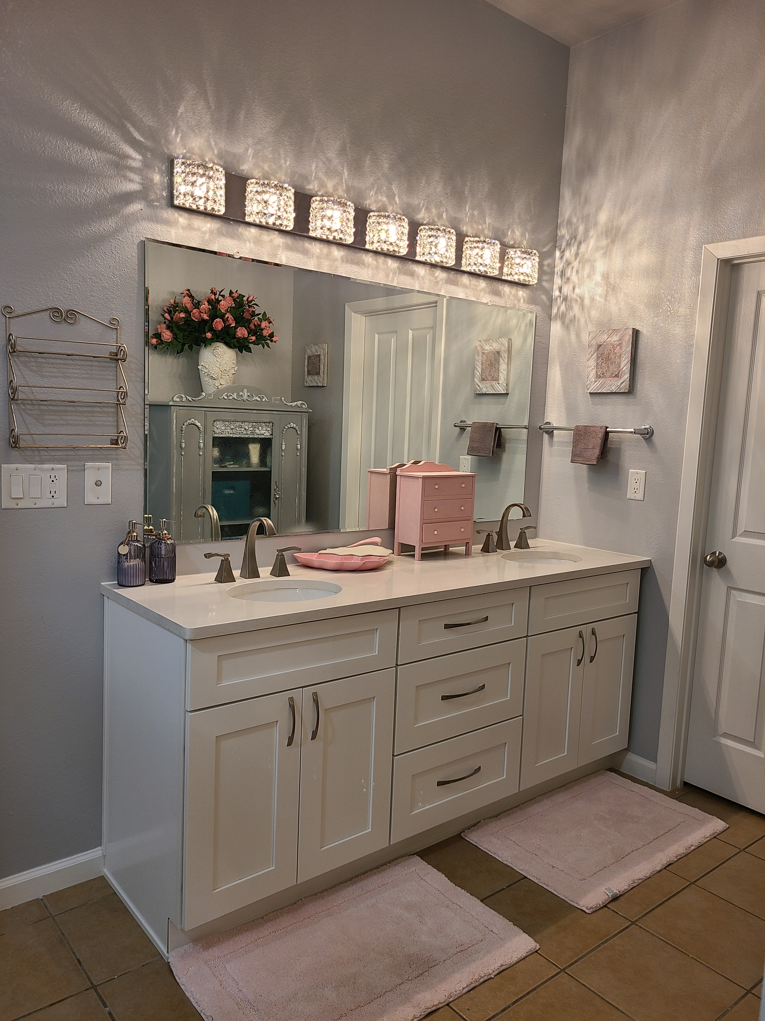 Elegant white double vanity with a crystal light bar, large mirror and soft pink accents
